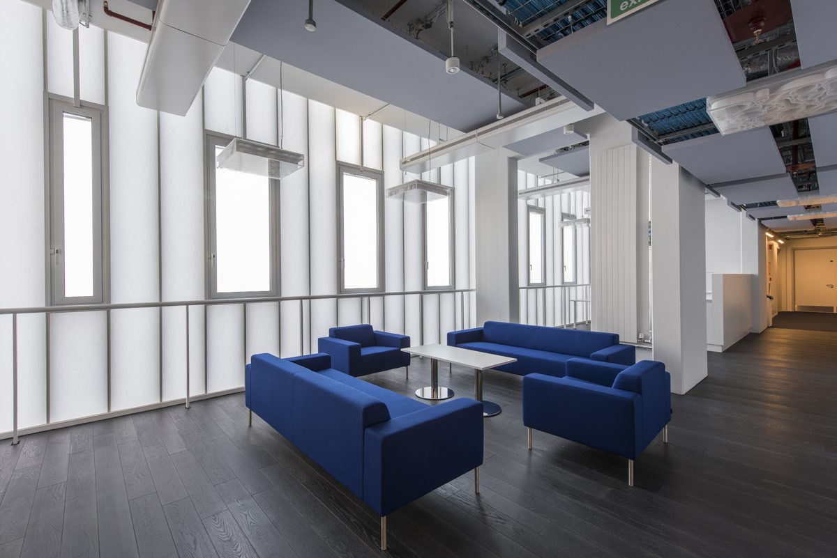 Interior view of a modern seating area featuring blue sofas and a coffee table, with large windows allowing natural light.
