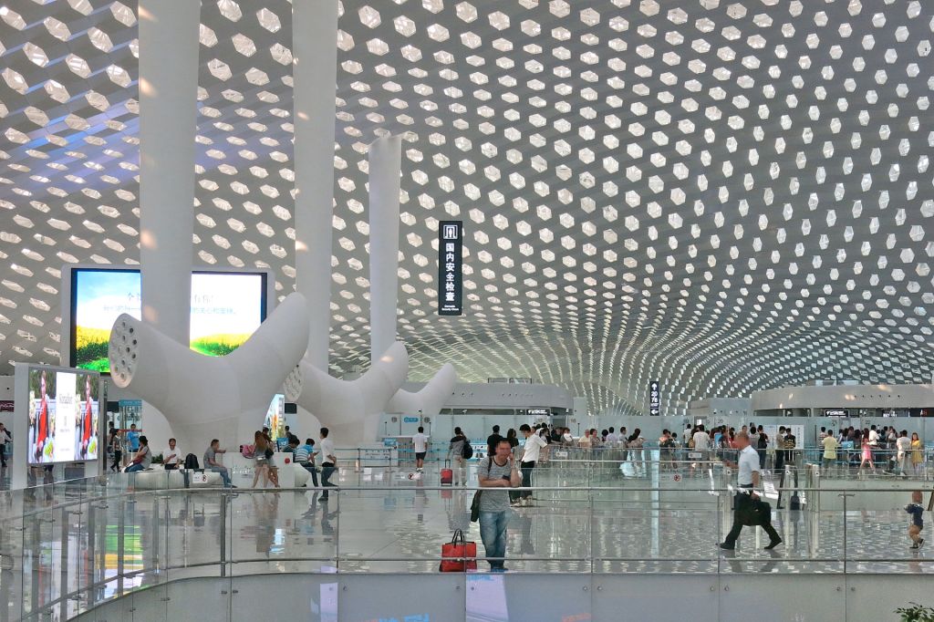 Interior view of a modern architectural space featuring a unique patterned ceiling and numerous people interacting in a bustling environment.