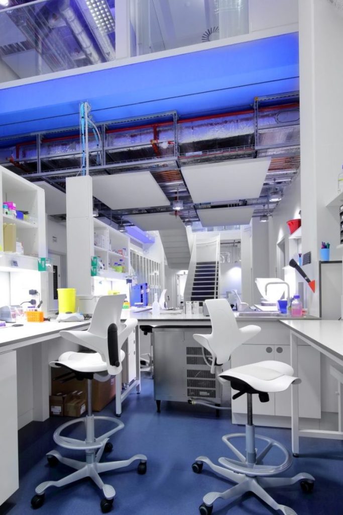 Interior of a modern laboratory with white countertops, adjustable stools, and a blue lit ceiling, showcasing a clean and functional design.