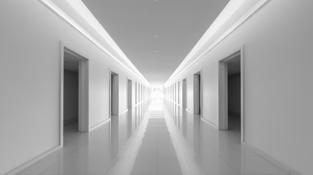 A long, symmetrical corridor with doors on either side and a bright light at the end, featuring sleek white walls and a polished floor.