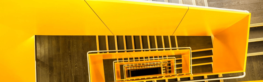 A top-down view of a modern staircase with bright yellow walls and wooden steps, showcasing a geometric design.