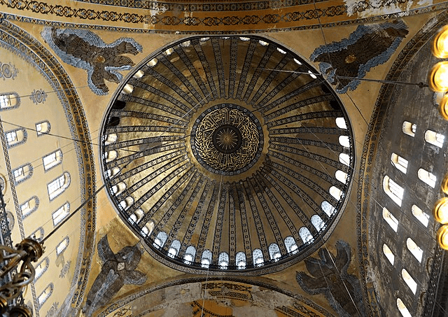 Vista desde abajo del domo de una iglesia, mostrando decoraciones doradas y elementos arquitectónicos en la cúpula.