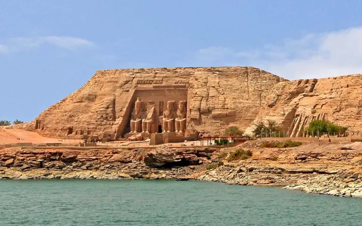 Vista de los templos de Abu Simbel en Egipto, tallados en la roca, junto a un lago en un día soleado.