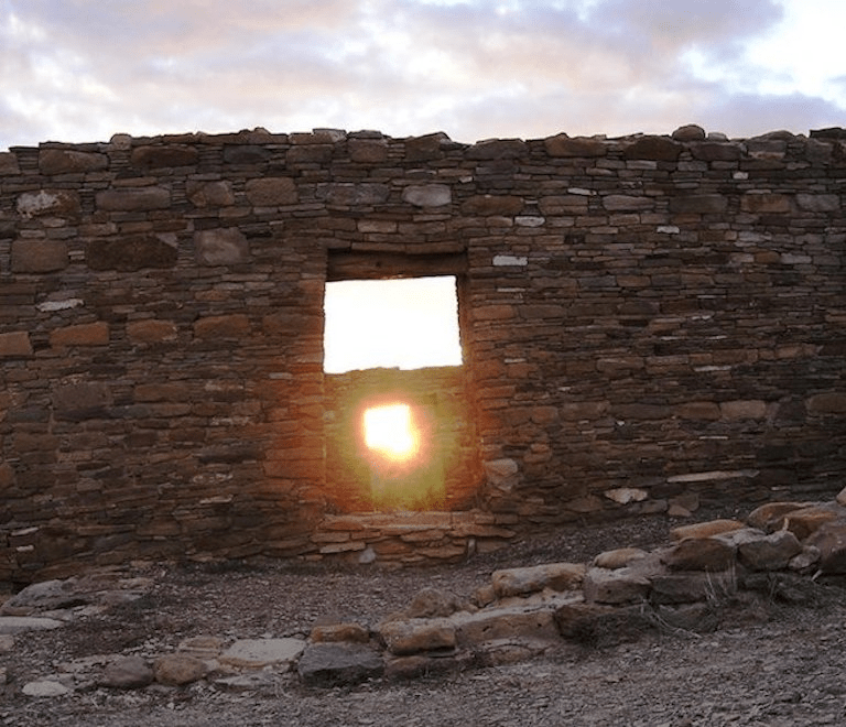 Vista de una ruina de piedra con una ventana por donde entra el sol poniente, simbolizando la conexión entre la arquitectura ancestral y la luz.