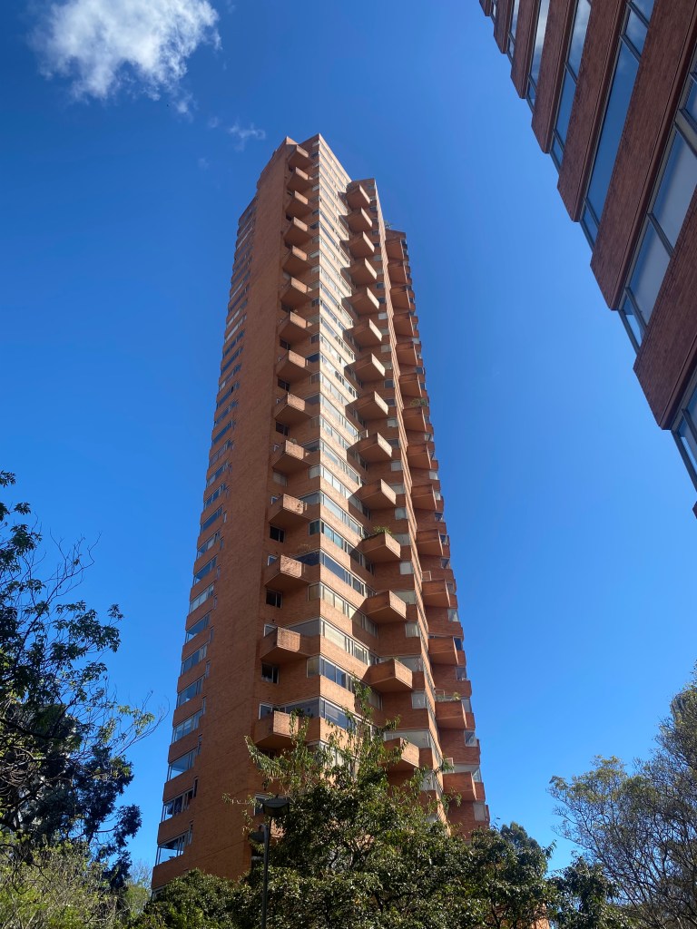 A tall residential tower with balconies, against a clear blue sky.