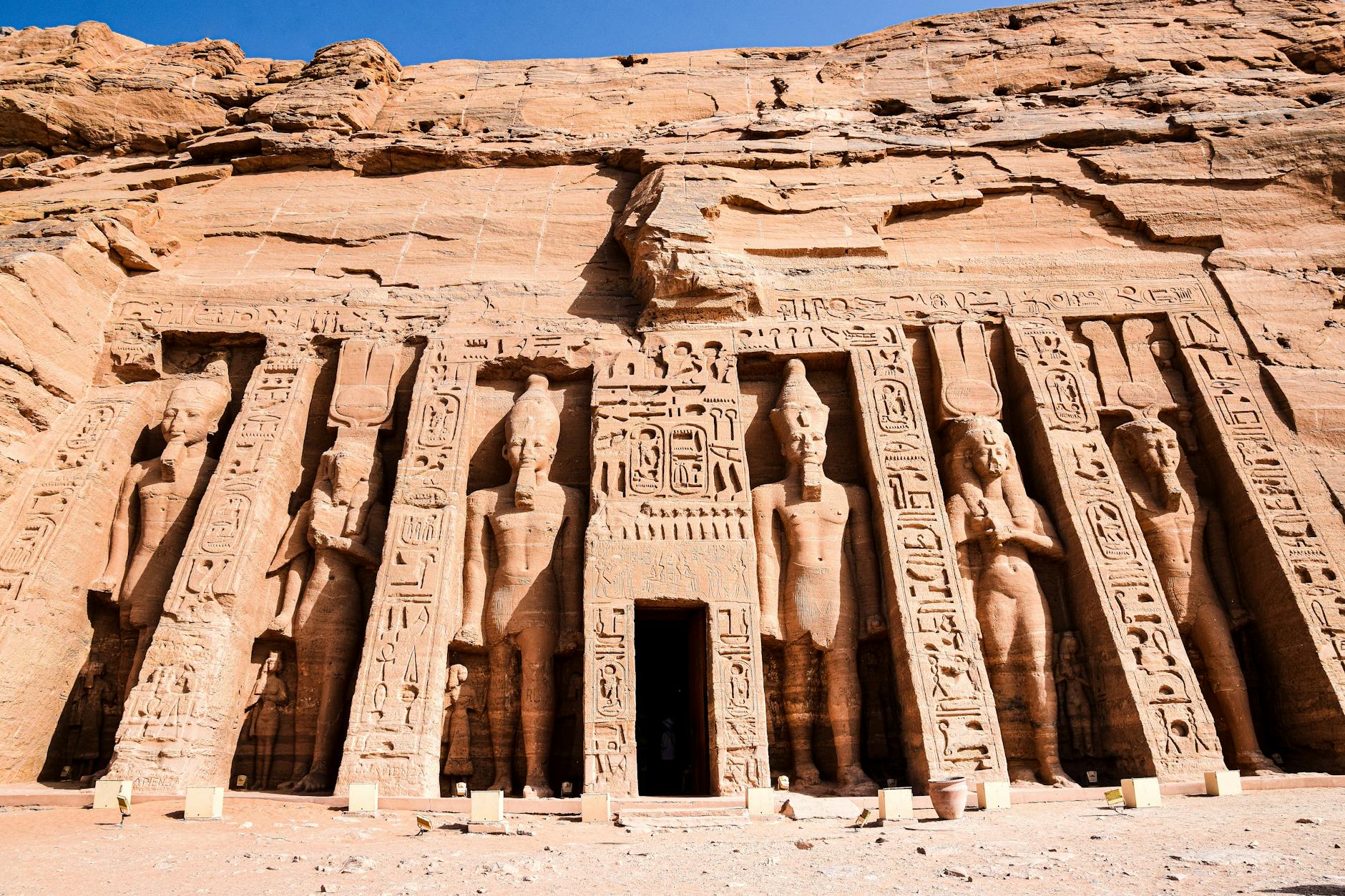 Fachada del templo de Abu Simbel en Egipto, con impresionantes estatuas esculpidas en piedra que representan a deidades y faraones, rodeadas de grabados jeroglíficos.