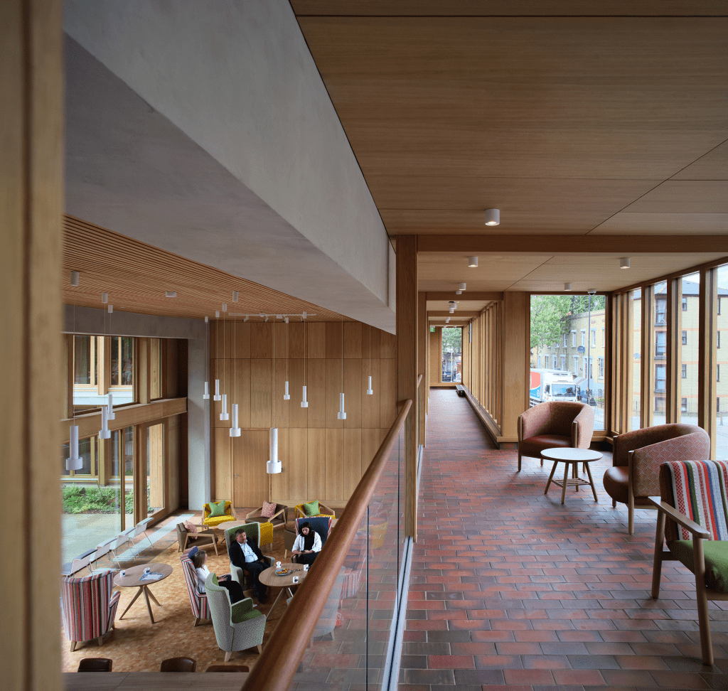 Vista interior del Appleby Blue Almshouse, mostrando un pasillo amplio con muebles modernos y zonas de descanso, donde se observa a residentes interactuando en un ambiente luminoso y acogedor.