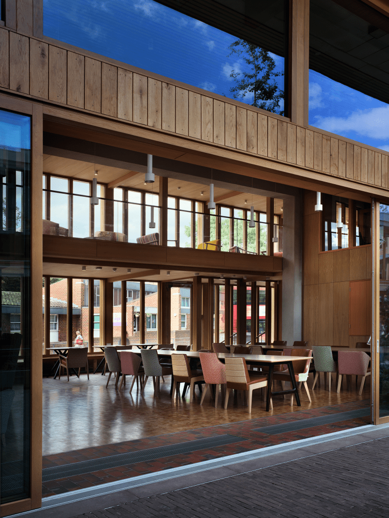 Vista del interior del Appleby Blue Almshouse, mostrando un salón con mesas y sillas de diseños variados y amplias ventanas que permiten la entrada de luz natural.