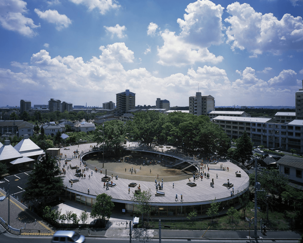 Aerial view of Fuji Kindergarten in Tokyo, showcasing its circular design and outdoor play area surrounded by greenery, with children playing and engaging in movement.