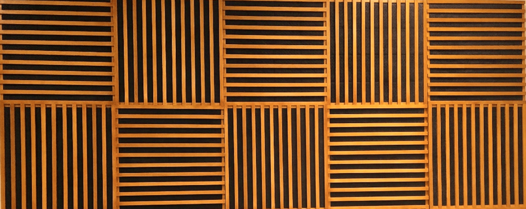 Panel de madera con listones que crean patrones geométricos en un fondo oscuro, utilizado para absorción acústica.