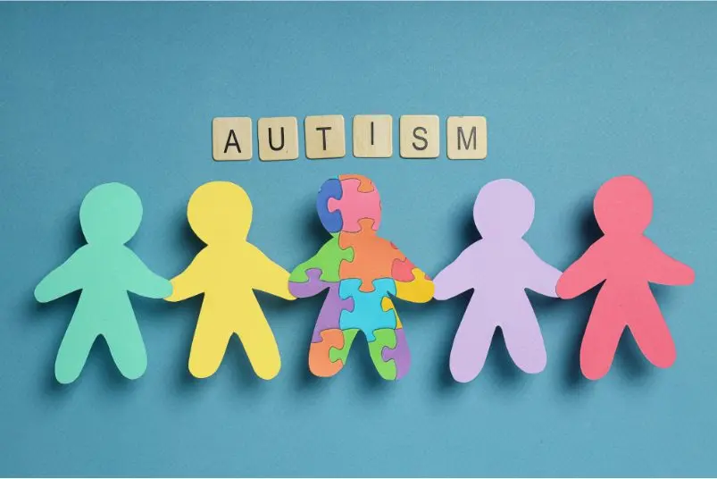 Colourful paper cut-out figures holding hands with letters spelling 'AUTISM' above them on a blue background.