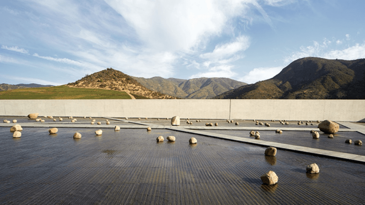A serene landscape featuring a smooth, stone surface with scattered rocks, overlooking rolling hills and mountains under a partly cloudy sky.