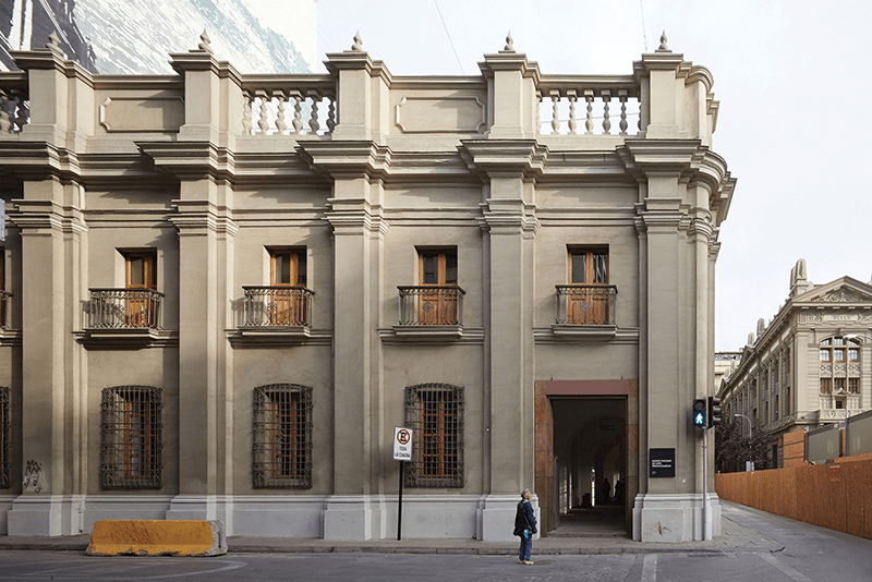 Historic building facade featuring tall windows with ornate balconies, situated on a city street with a pedestrian crossing signal in view.