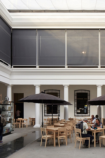 Interior view of a modern café with wooden tables and chairs, black umbrellas, and large windows, showcasing a relaxed atmosphere.