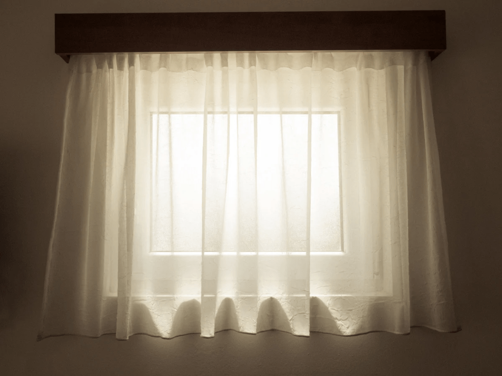 A softly lit window with sheer white curtains, allowing gentle light to filter through.